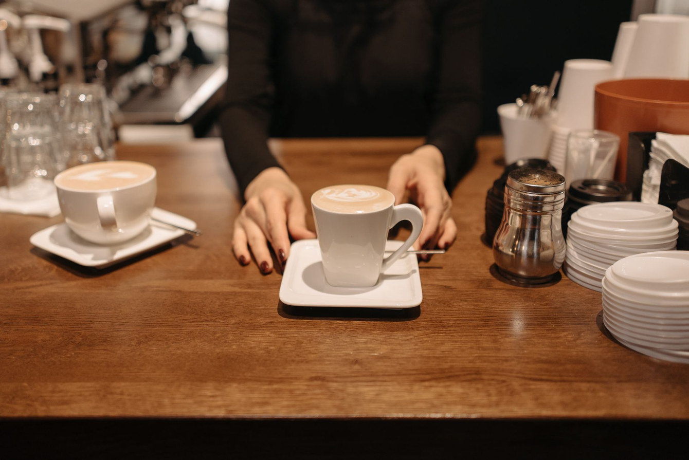 Hands setting unbranded coffee cups on a service counter.