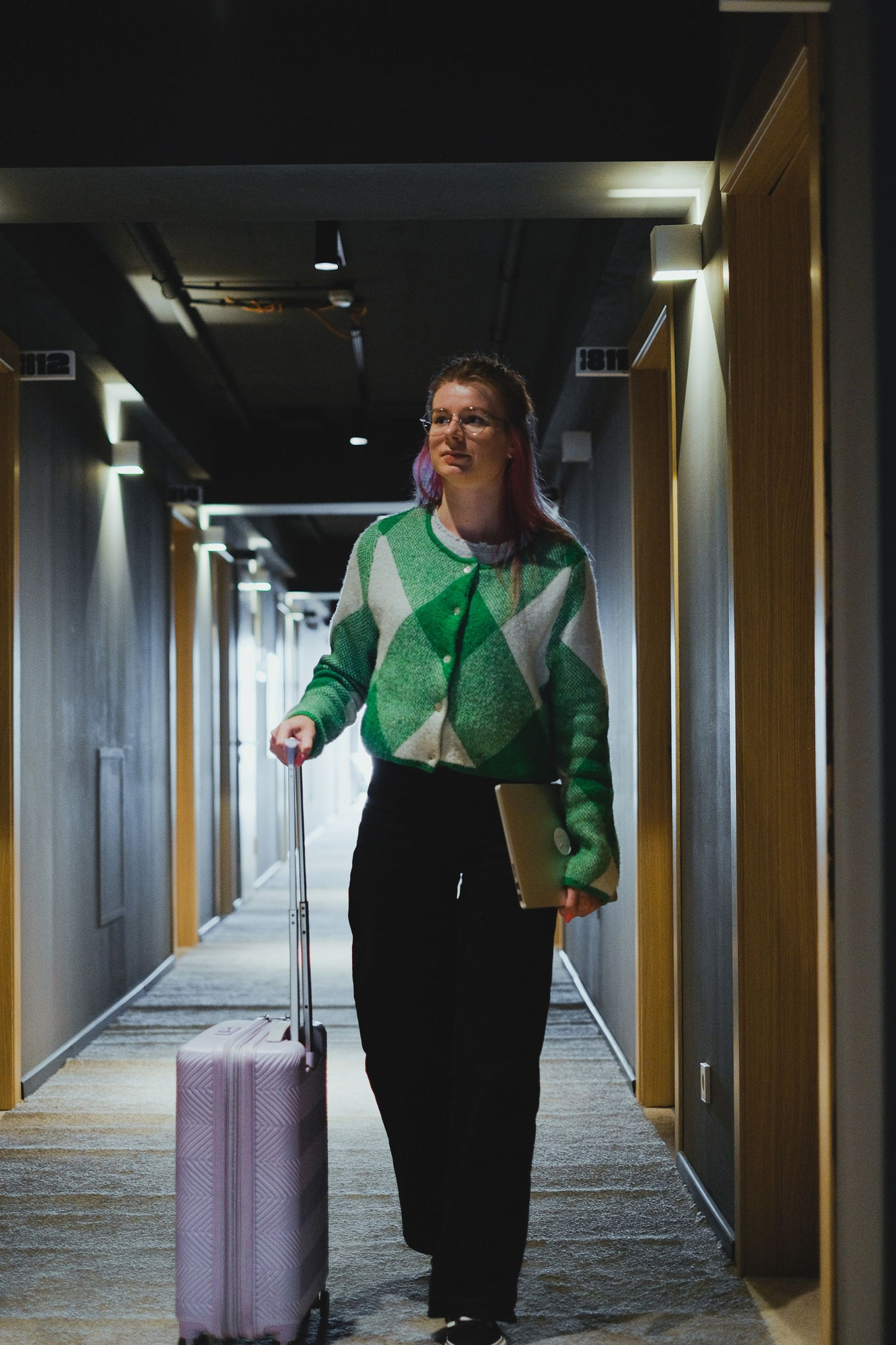 A guest walking the corridor to her room, luggage in hand, at the start of a stay.