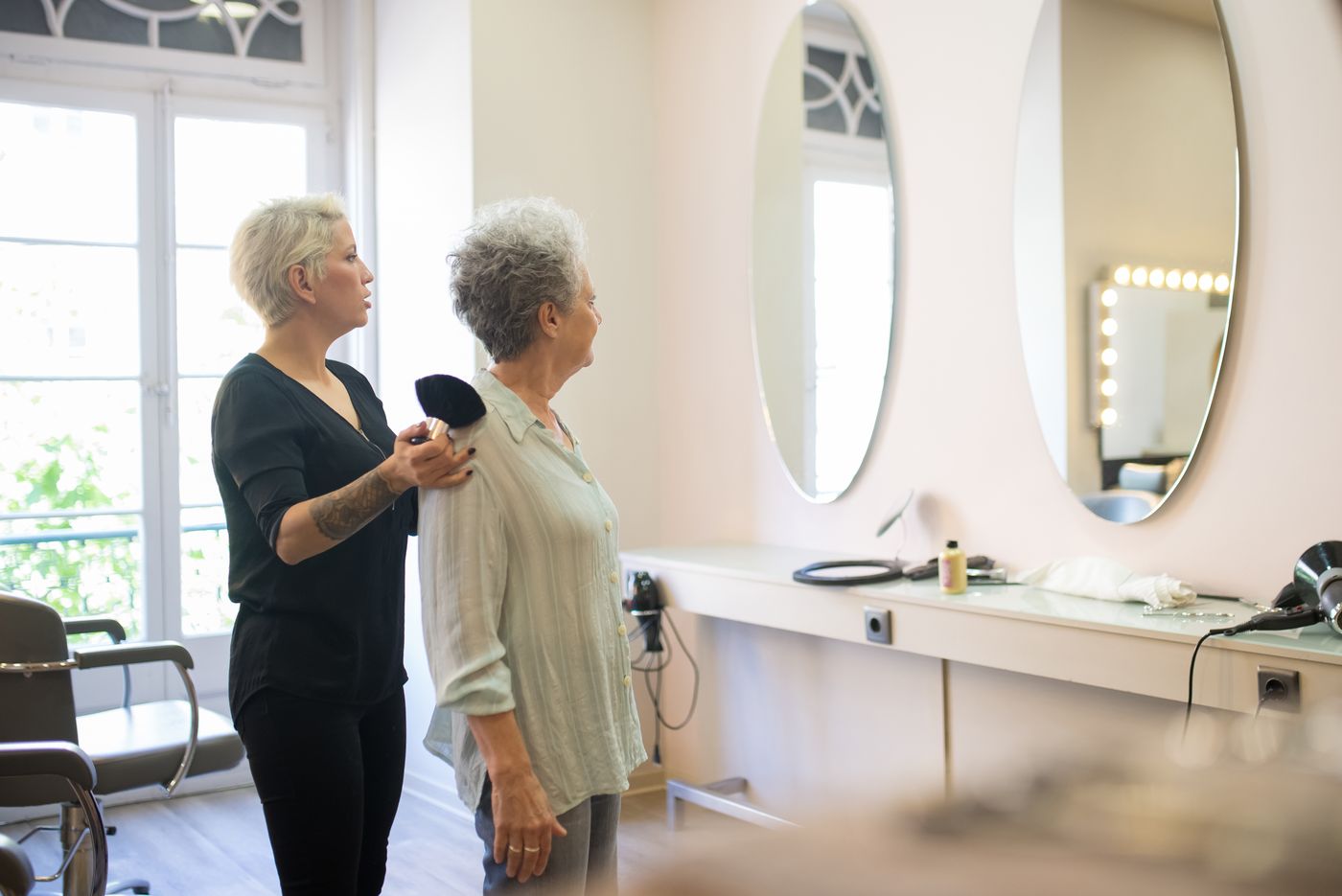 A client and stylist at a salon mirror — a relationship, not a transaction.