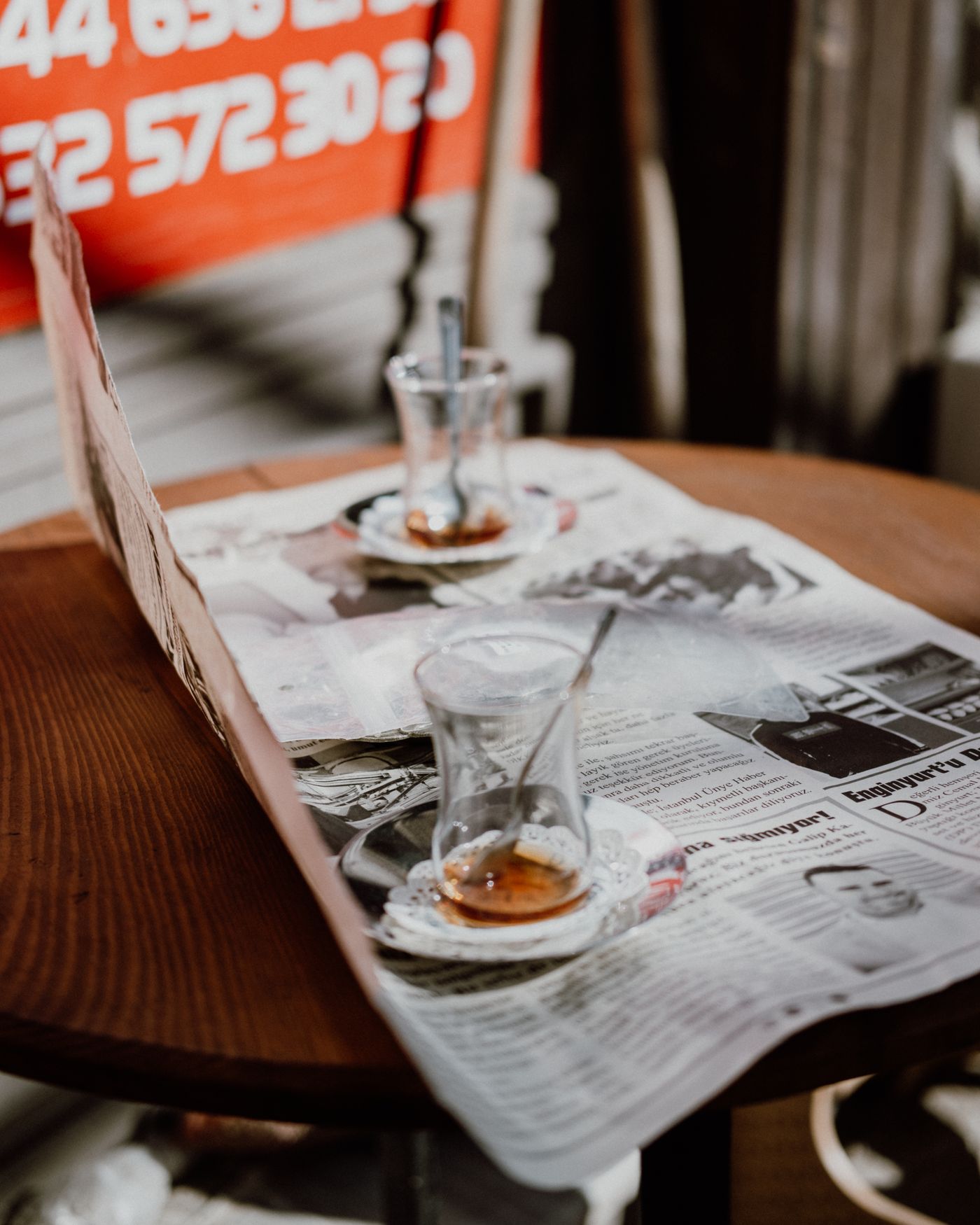 Two glasses of tea and an open newspaper left on a café table after a long sit.