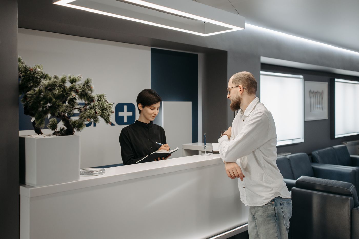 A patient waiting at a clinic reception desk while the appointment is written up.