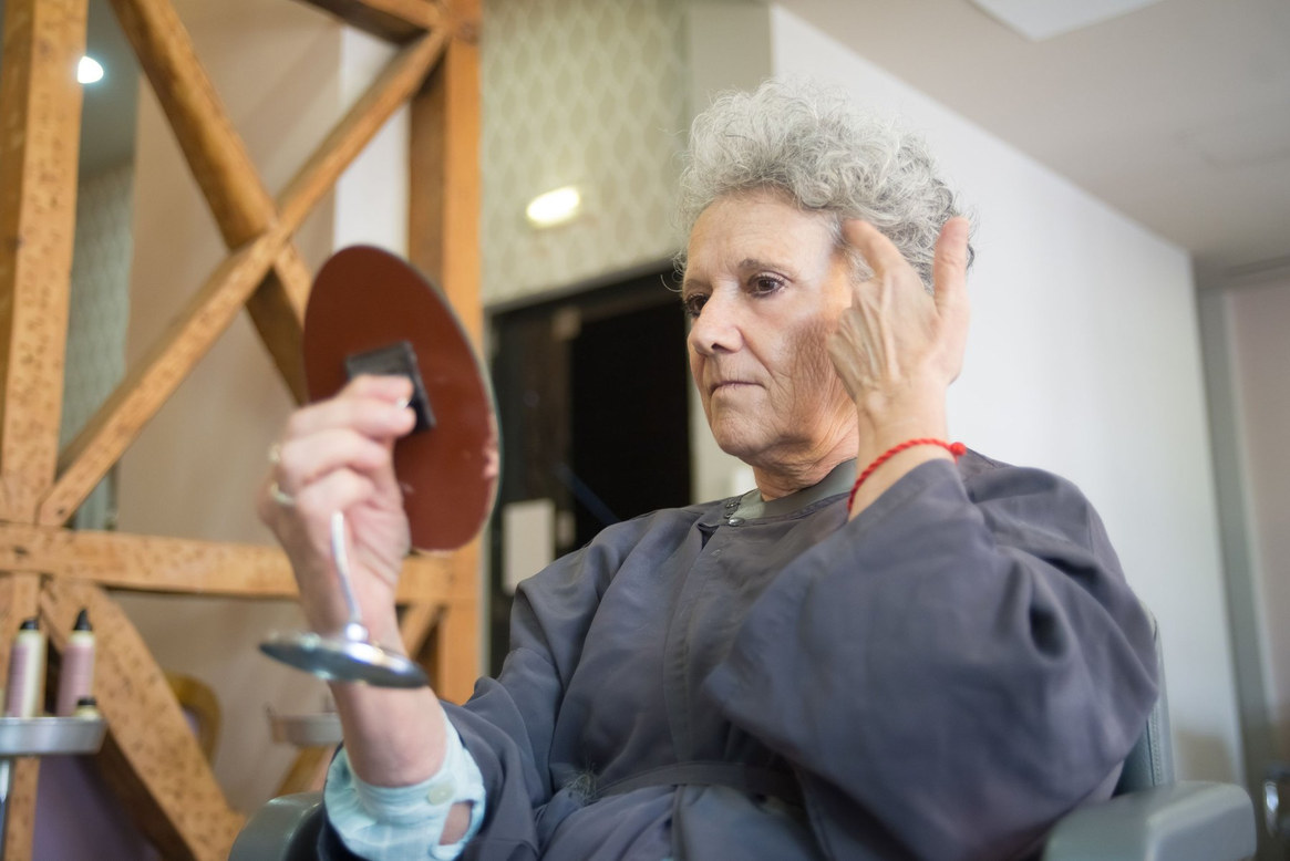 A salon client raises a hand mirror to check the finished result, her other hand still at her hair.