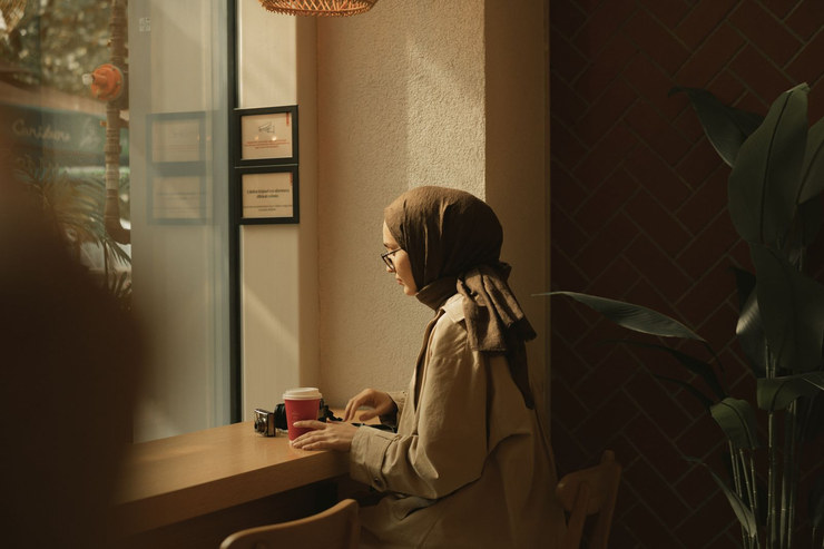 A woman at a café window counter, quietly finishing her coffee.